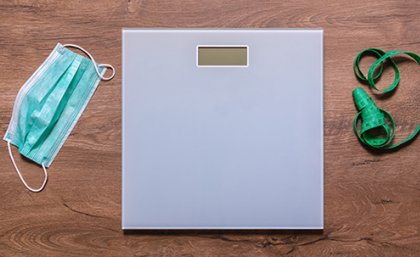A weighing scale on a wooden floor next to a tape measure and a surgical face mask